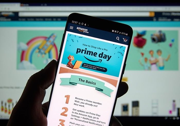 Hand håller en mobil med Amazon Prime Day-sida framför en datorskärm