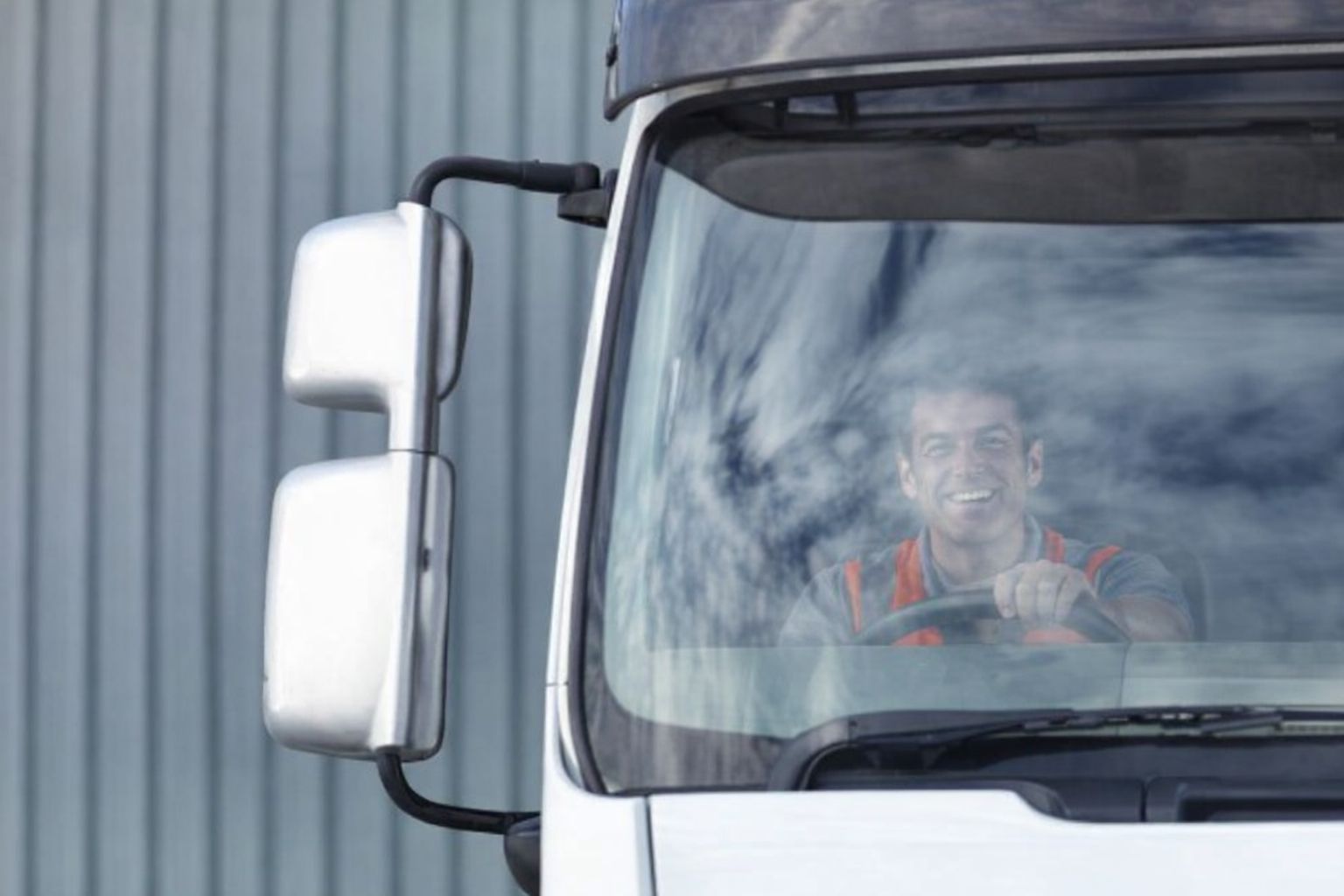 Leende lastbilsförare med orange väst syns genom framrutan på en lastbil.