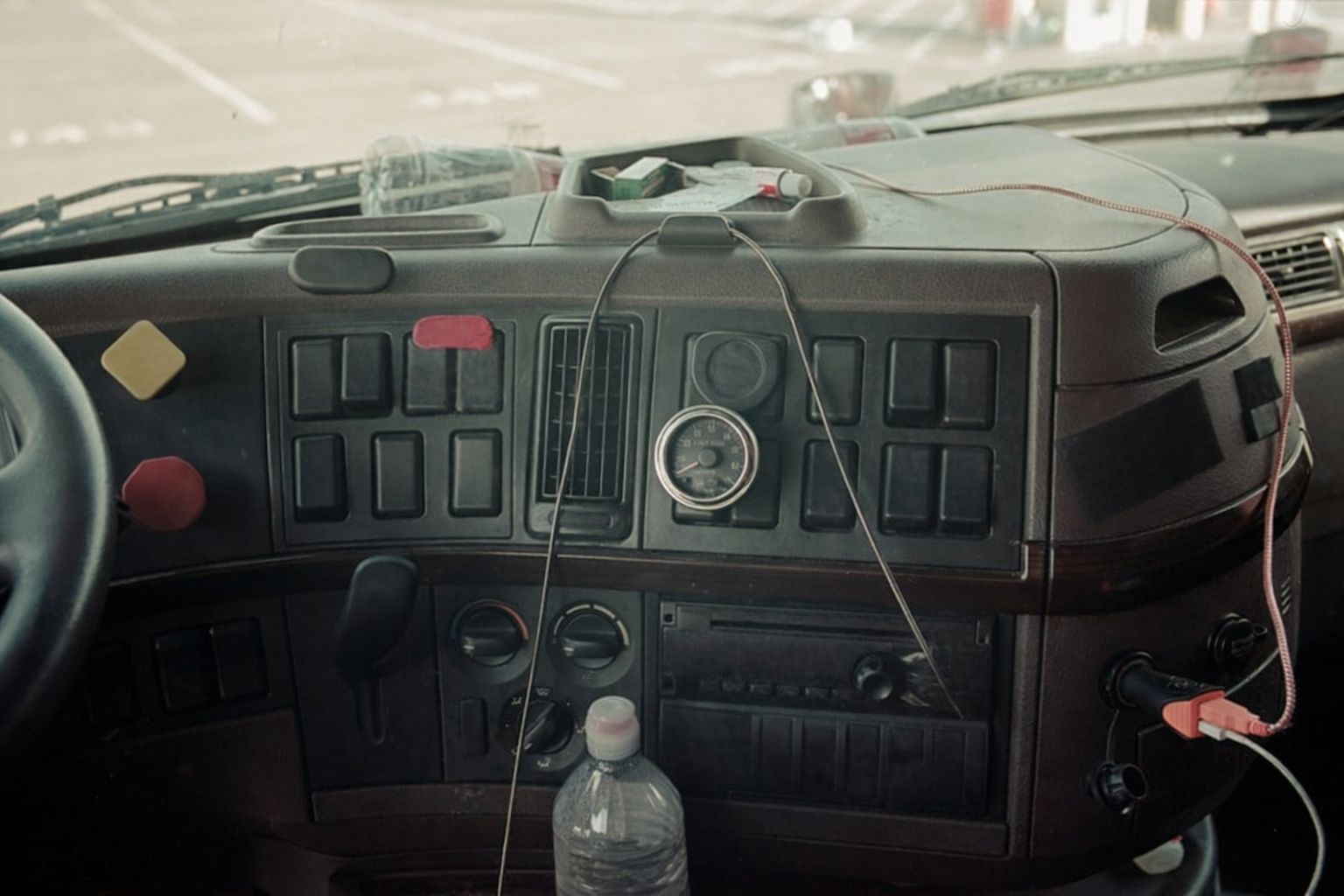 Instrumentbräda i en lastbil med ratt, knappar och en flaska vatten.