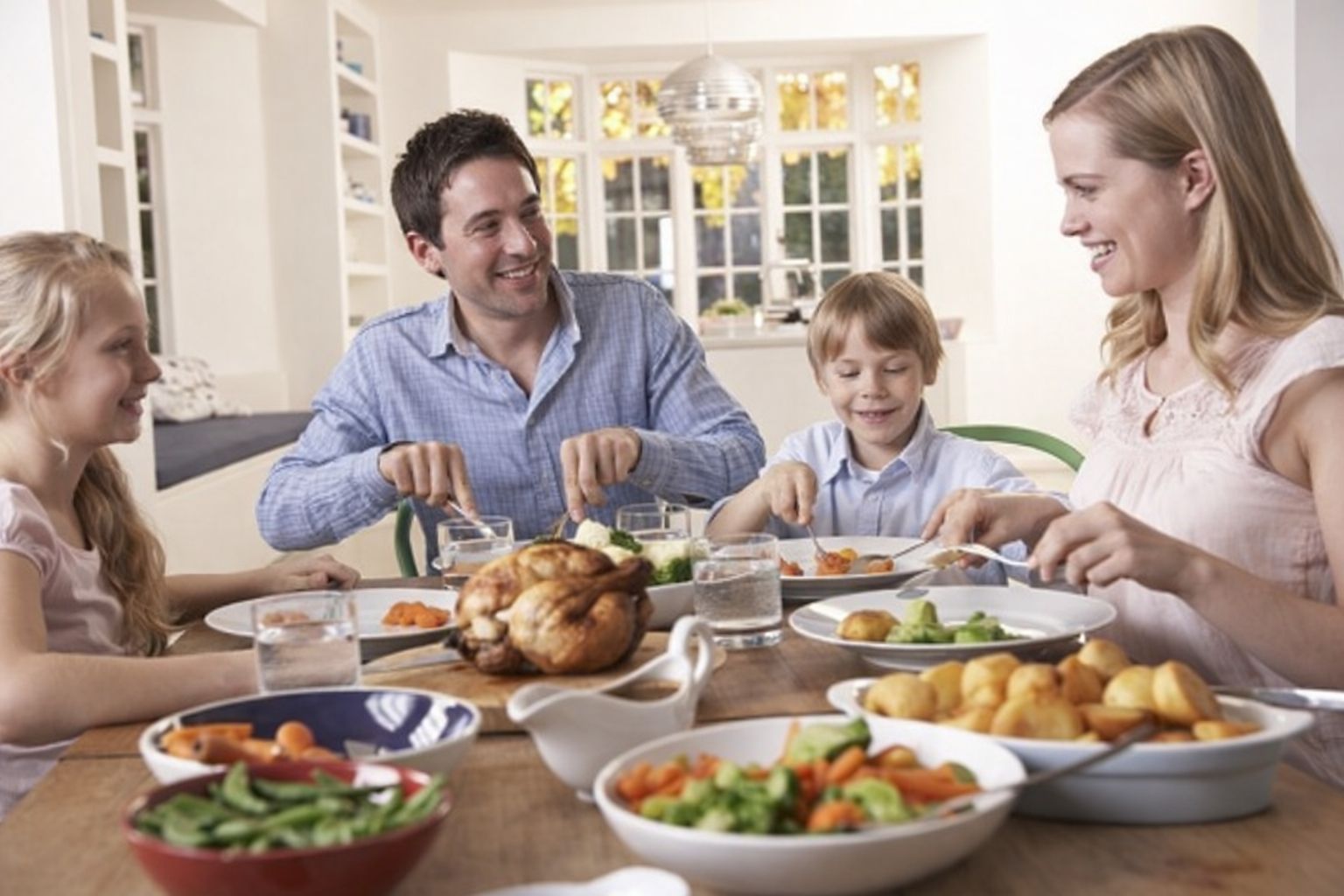 Familj äter middag tillsammans, med en hel kyckling och grönsaker på bordet.