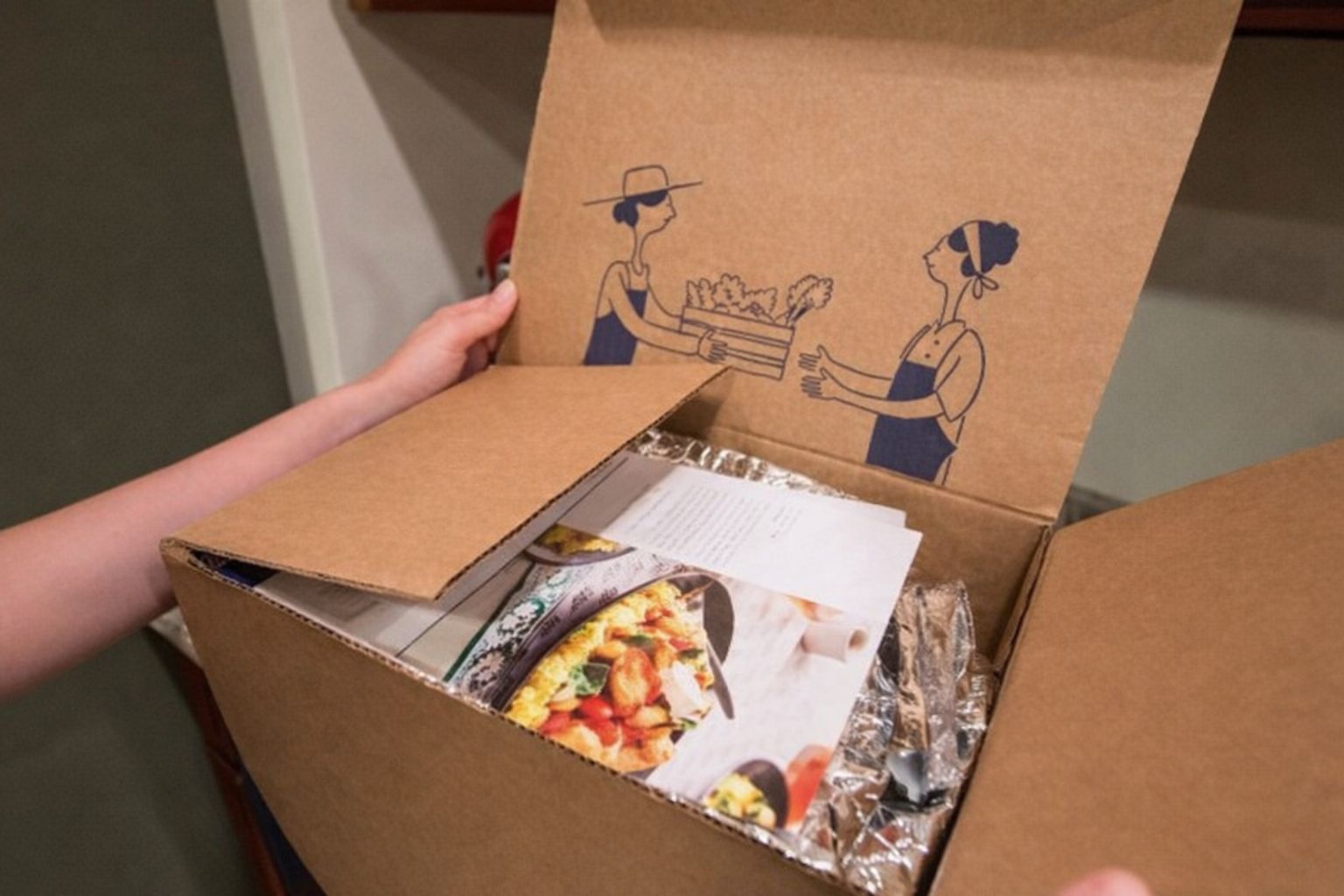 Öppen matkasse med recept, inplastade ingredienser och illustrationer på insidan